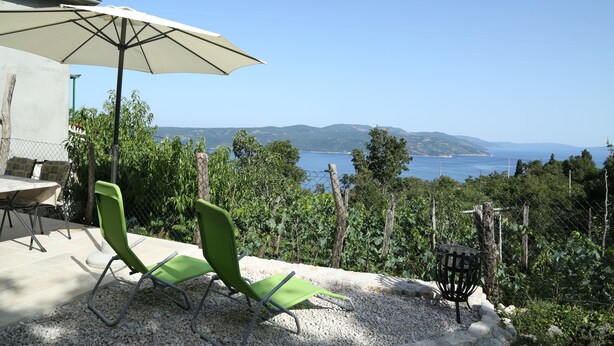Un patio con mesa, sillas y sombrilla que ofrece vistas panorámicas del mar y las montañas.