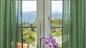 Una ventana con cortinas verdes, una planta en maceta y una orquídea púrpura.