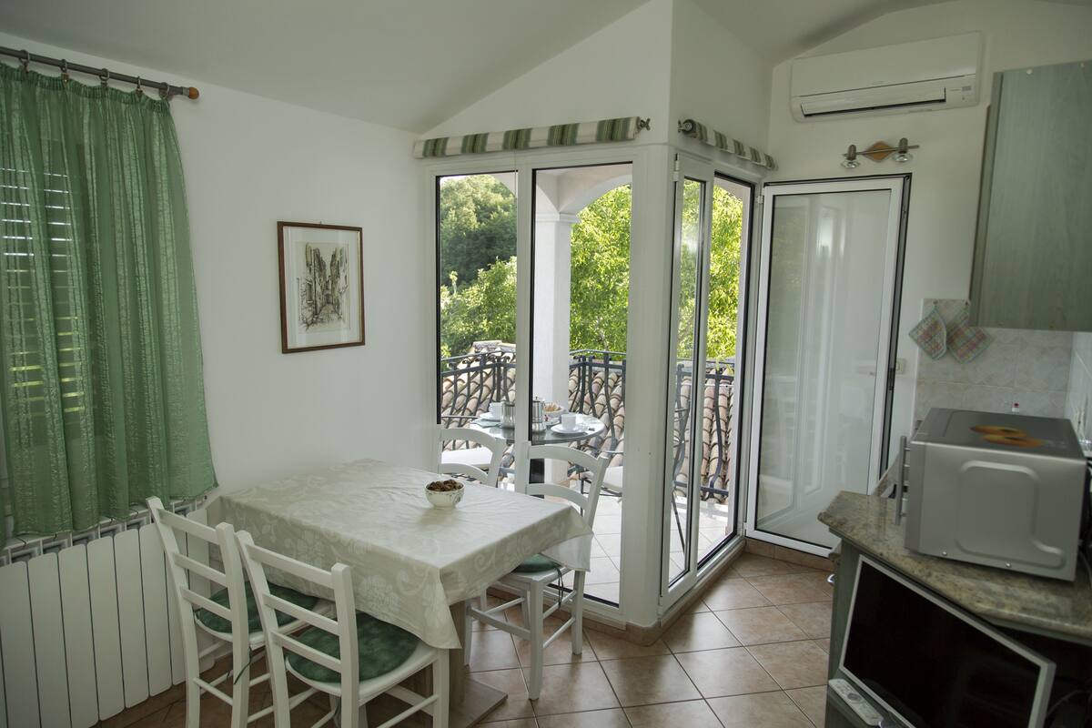 Een eethoek met een tafel en stoelen, uitzicht op het omliggende landschap, een keuken met een magnetron en een schuifdeur van glas.
