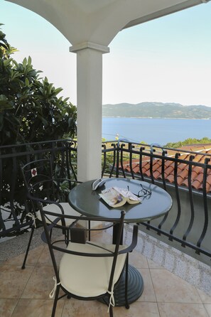 A round table with a chair, a book, and glasses on it, set on a balcony with a view of the sea and mountains. - Apartments Tinka (Moscenicka Draga)