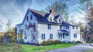 A large, two-story house with a steeply pitched roof, multiple windows, and a chimney.