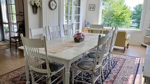 A dining area with a white table and chairs, surrounded by a patterned rug, with a view of greenery outside.