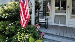 A house with a porch, an American flag, a bench, and a door labeled "199".