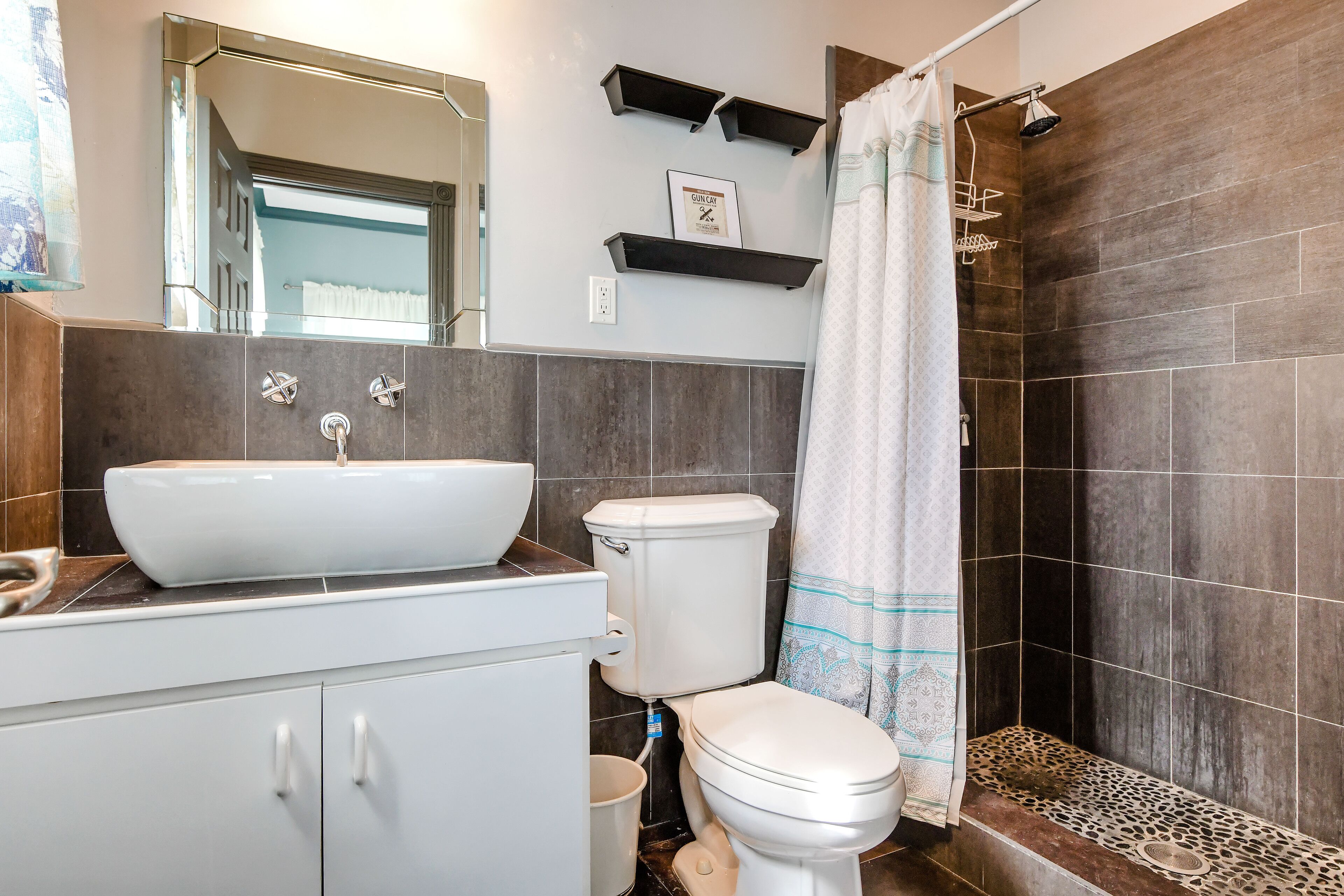 Ein modernes Badezimmer mit einem großen, weißen Waschbecken, einer Toilette und einer Duschkabine mit dunklen Fliesen.