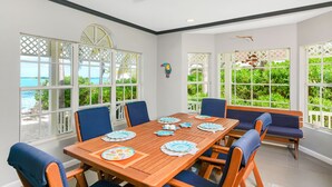 A dining area with a wooden table set for six, surrounded by blue upholstered chairs. - 11 steps to the Ocean  (George Town)