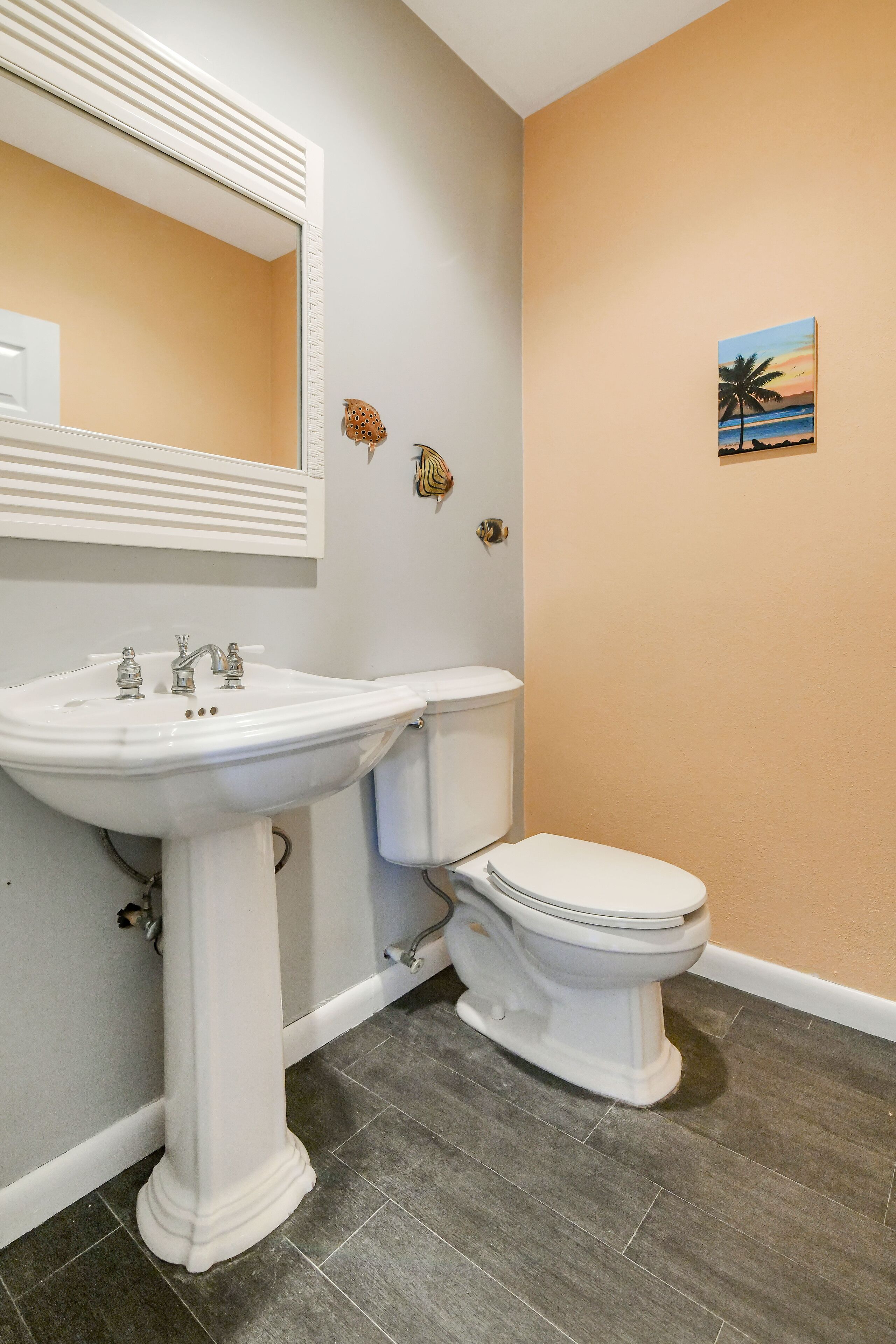 A bathroom with a pedestal sink, toilet, and a wall-mounted mirror.