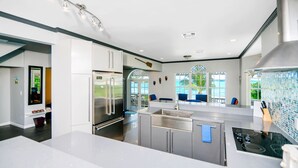 A modern kitchen with stainless steel appliances, a large island, and a view of the outdoors through large windows. - 11 steps to the Ocean  (George Town)