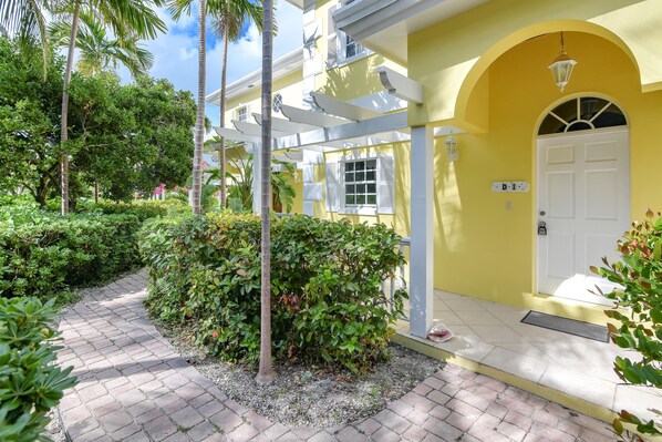 A yellow building with a white door labeled "D-1" and a covered walkway. - 11 steps to the Ocean (George Town)