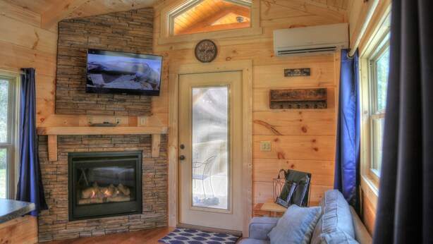 Un interior acogedor de cabaña con chimenea de piedra, televisor montado y techo de madera.