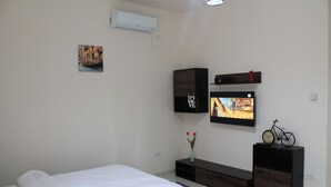 Un dormitorio moderno con cama, televisor, un pequeño cuadro y un jarrón con flores.