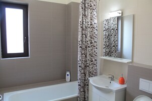 A bathroom with a bathtub, a sink, a mirror, and a window.
