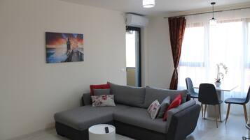 A modern living room with a grey sectional sofa, a round white side table, and a painting of a lighthouse on the wall.