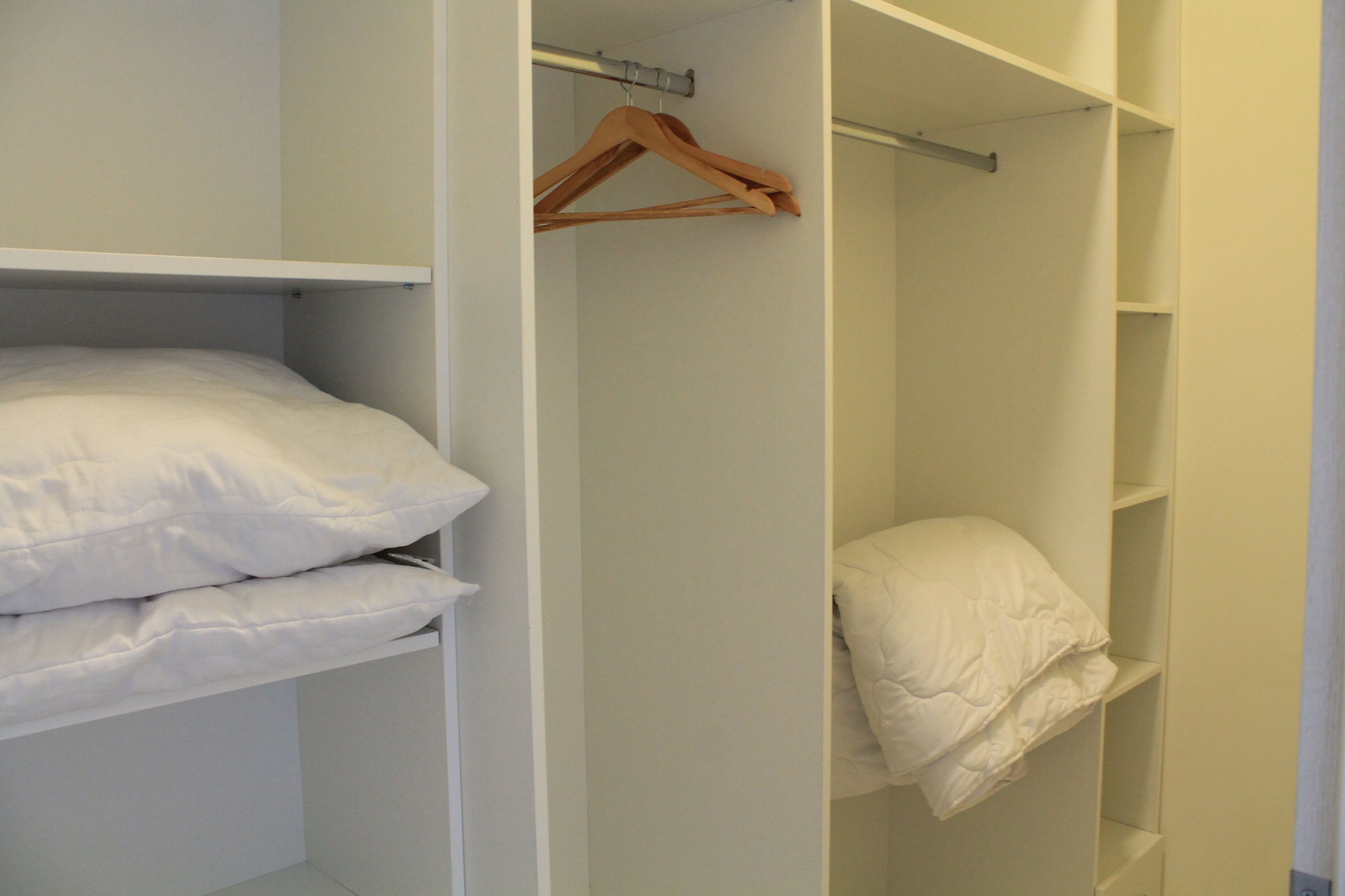 Un dressing avec des étagères blanches, un portant en bois et un lit avec une literie blanche.