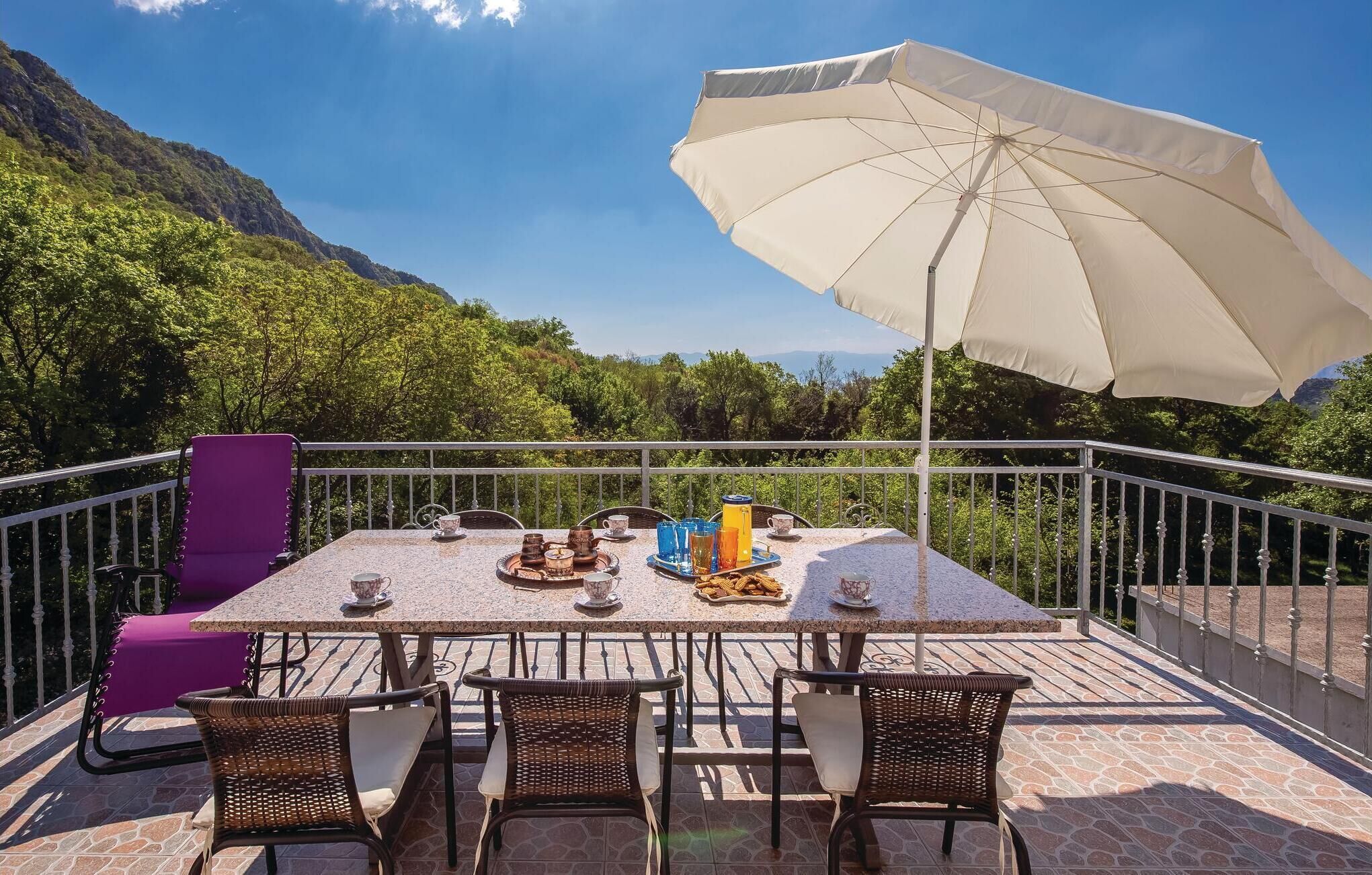 An outdoor dining area with a table set for four, surrounded by wicker chairs, a purple chair, and a large umbrella.