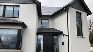 Une maison moderne à deux étages, avec une porte d’entrée noire, de grandes fenêtres et un petit porche.