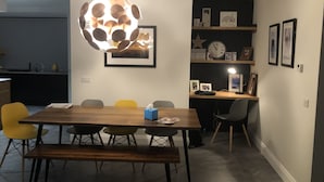 Un coin repas avec une table et des chaises en bois, un banc, un luminaire sphérique original et une bibliothèque avec des photos encadrées et une horloge.