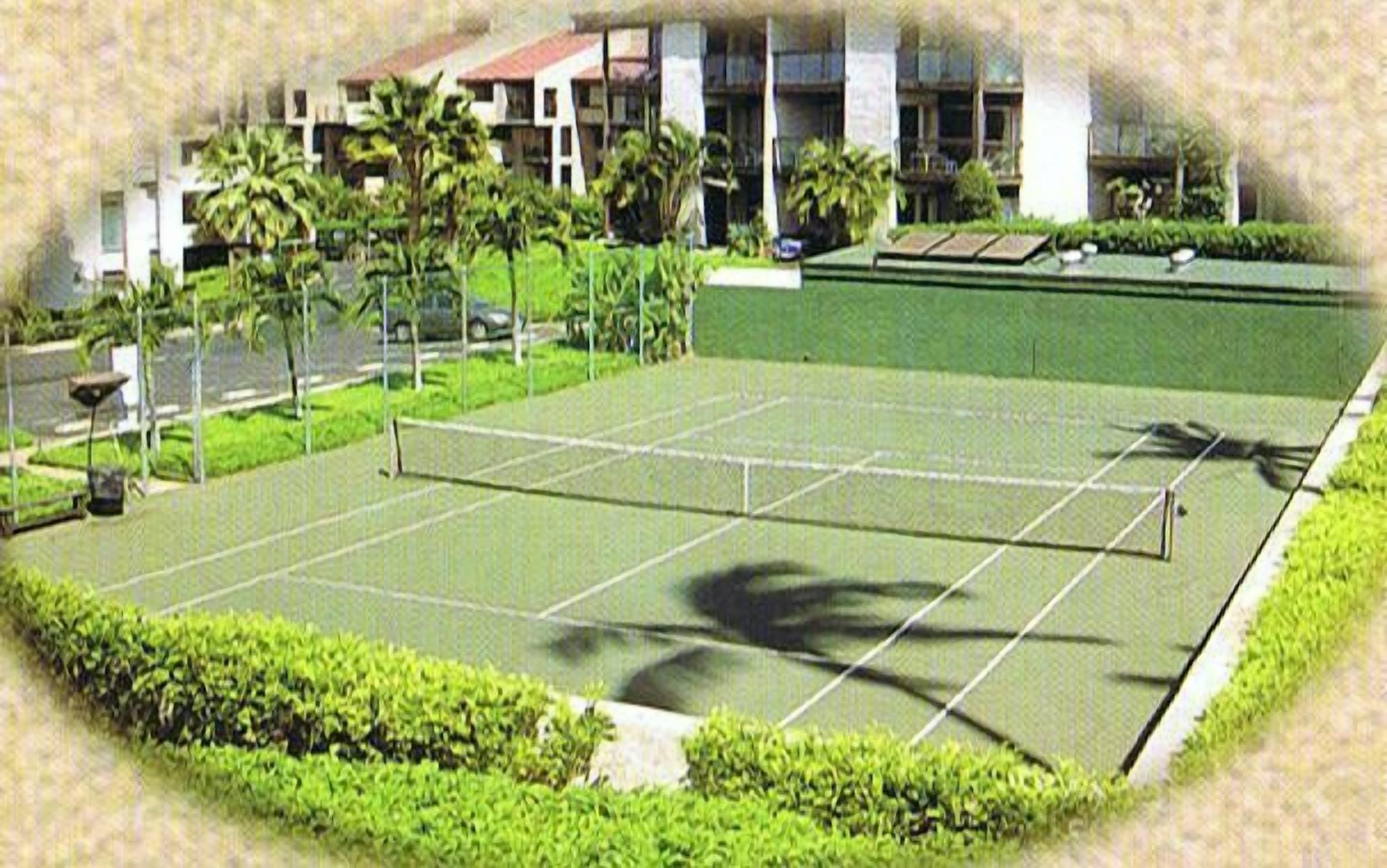 A tennis court surrounded by greenery and a building in the background.