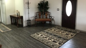 Une pièce dotée d’un parquet en bois foncé, d’un tapis à motifs, d’un banc en bois, d’un porte-manteau et d’une porte avec un luminaire.