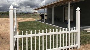 Une véranda couverte avec un barbecue, une cour clôturée et une vue sur le paysage environnant.