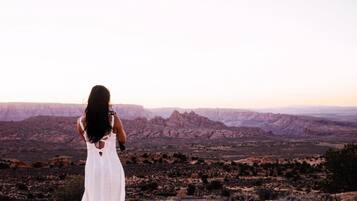 A person in a white dress standing on a hill overlooking a vast canyon landscape.