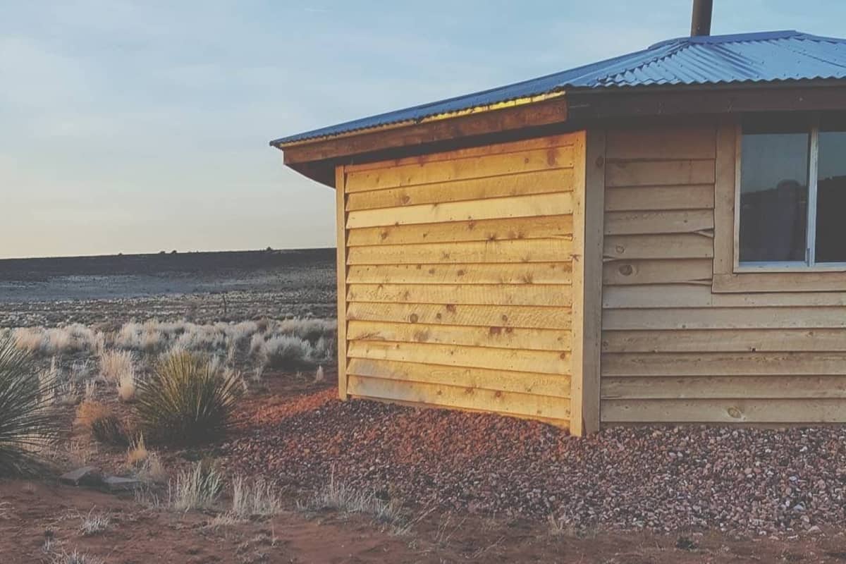 A wooden cabin with a metal roof, situated in a dry, grassy landscape.
