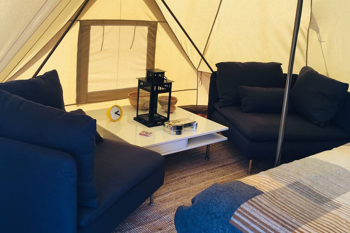 A tent with a bed, a table with a lantern, and two sofas.