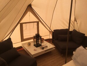 A cozy tent interior with a sofa, a small table with a clock, and a lantern.
