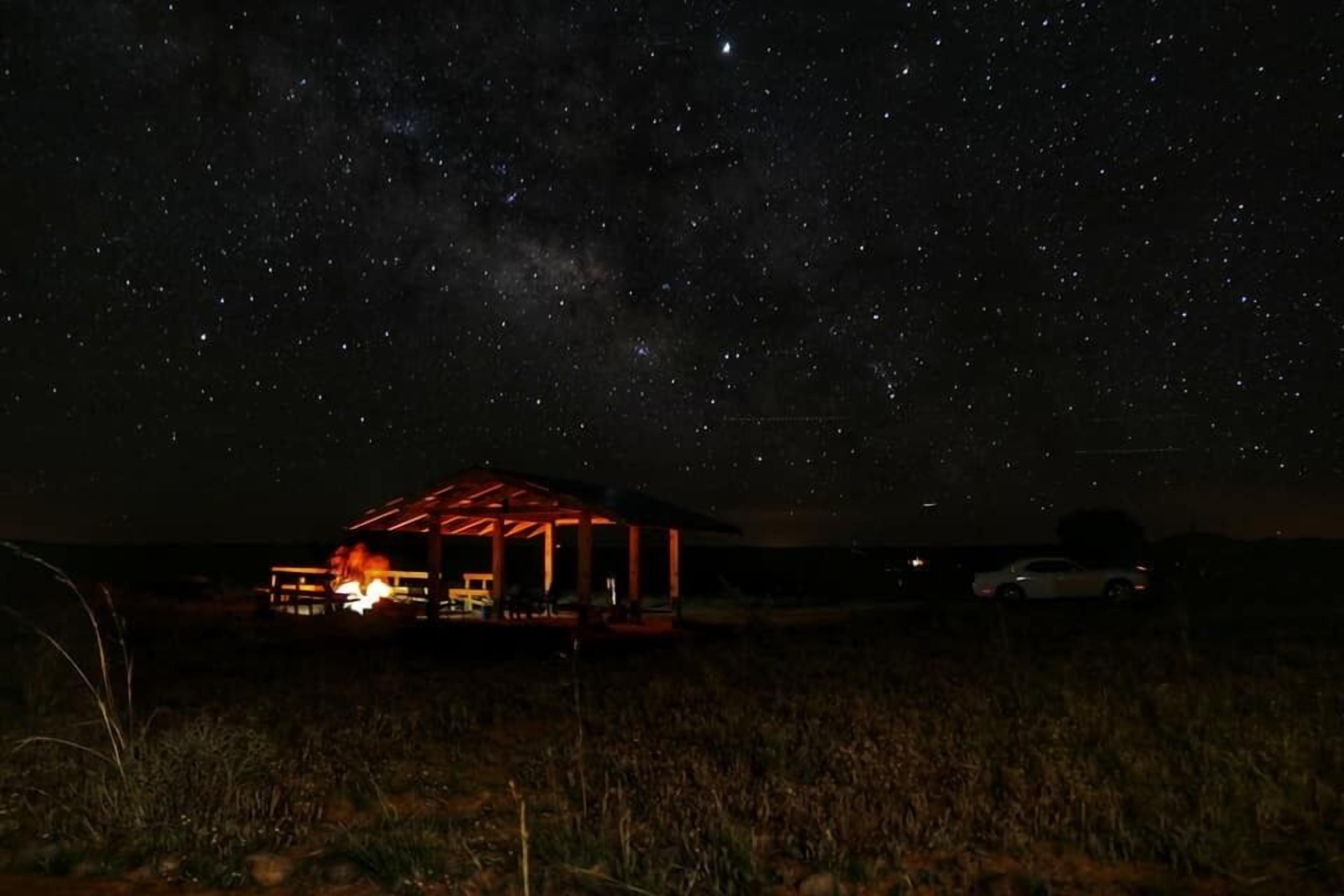 A starry night sky with a building featuring a covered outdoor area and a car parked nearby.