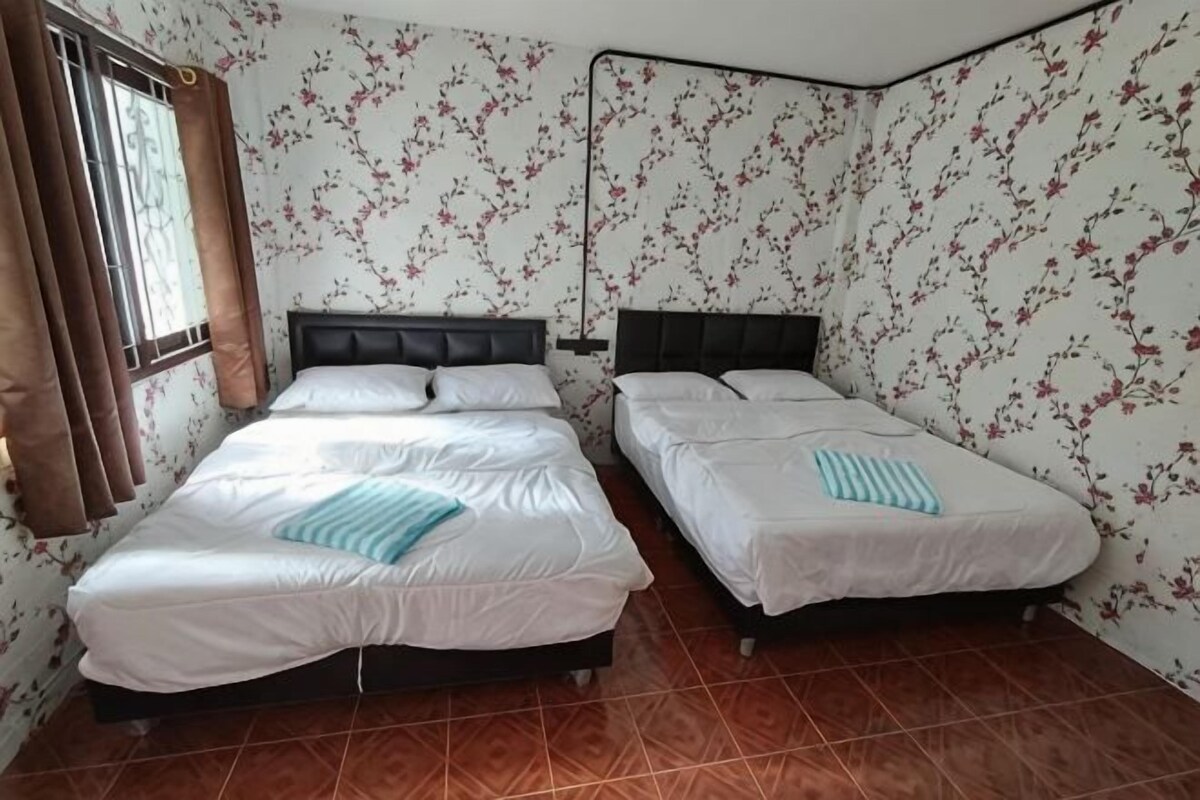 A room with two beds, a window with curtains, and floral wallpaper.
