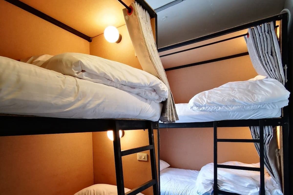 A bunk bed room with two beds, a wall socket, and a small trash bin.