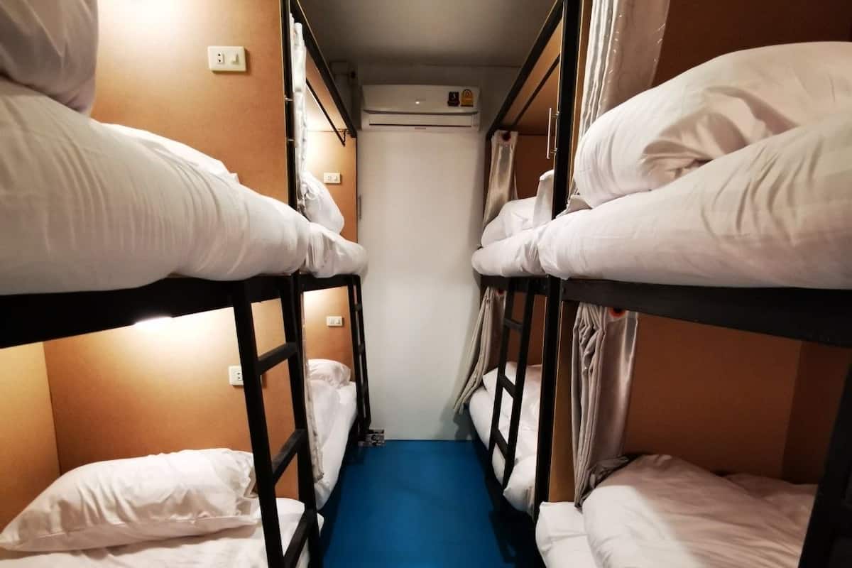 A narrow corridor with bunk beds on either side, a blue carpet, and a white wall with a power outlet.