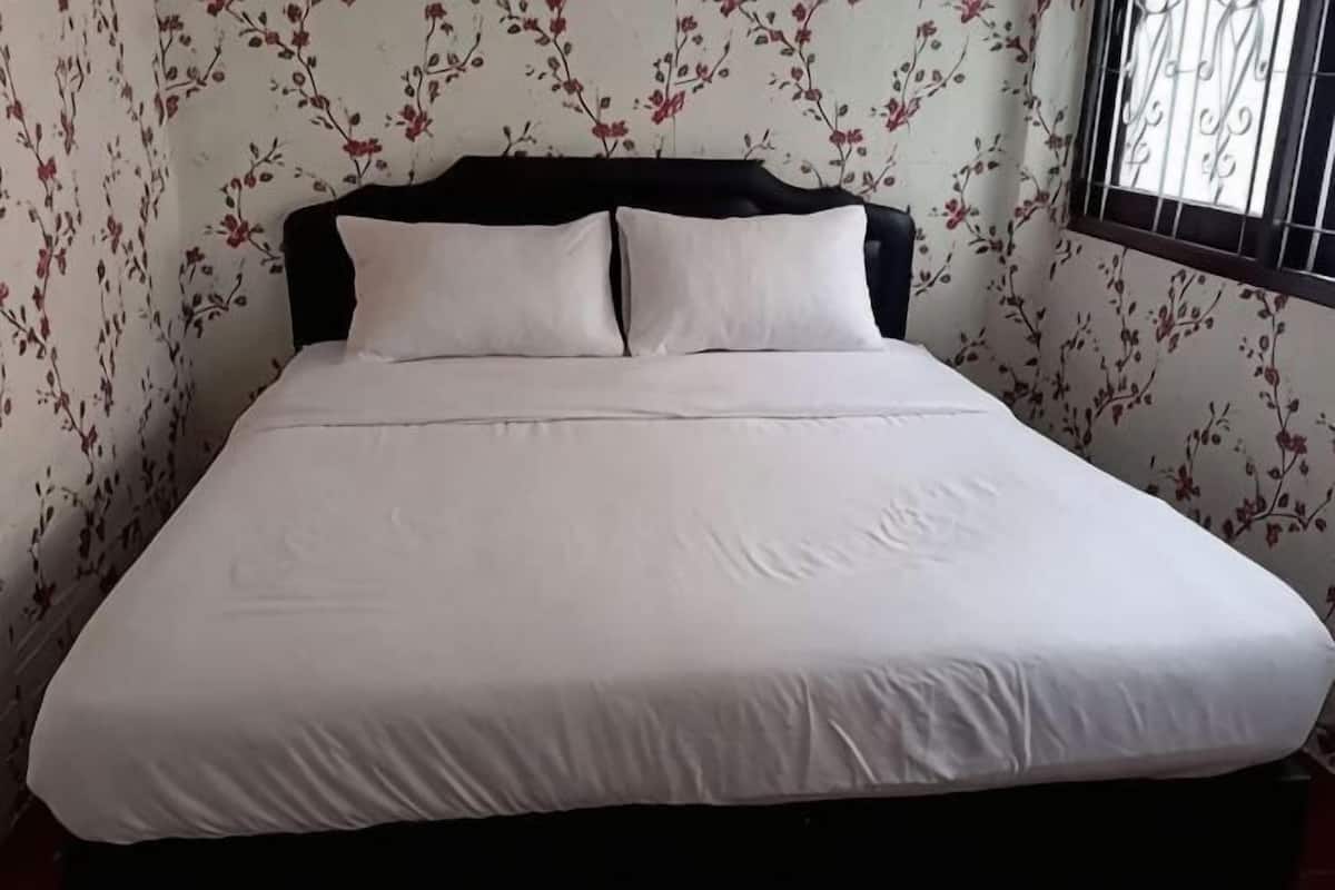 A bed with white bedding, a dark headboard, and floral wallpaper.