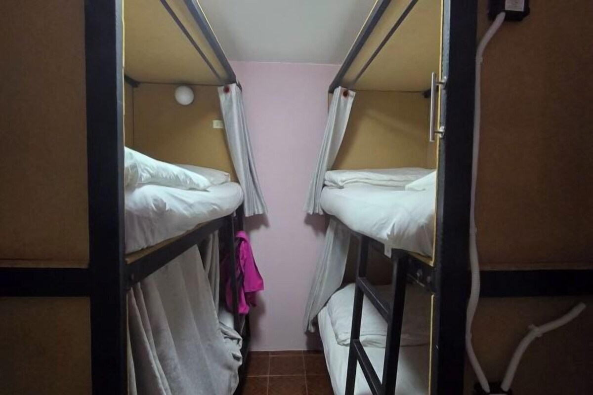 A narrow room with bunk beds, a pink wall, and a visible electrical outlet.