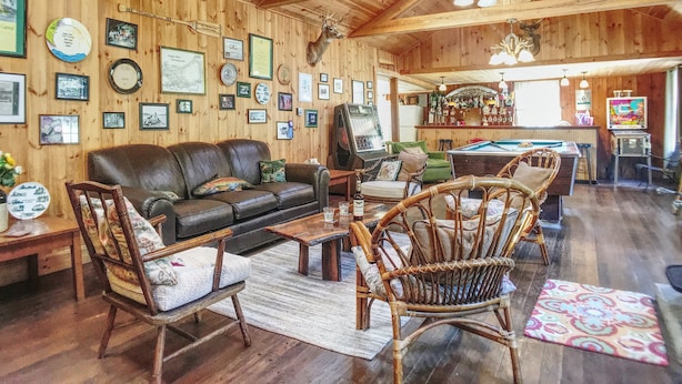 Un intérieur chaleureux, avec des boiseries, un canapé en cuir, des fauteuils en osier, une table de billard et un coin bar.