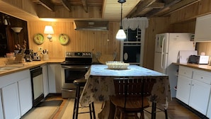 Une cuisine avec des murs en bois, un îlot central doté d’une table et de chaises, une cuisinière et un réfrigérateur.