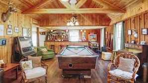 Un intérieur en bois avec une table de billard, des fauteuils verts et un coin bar.