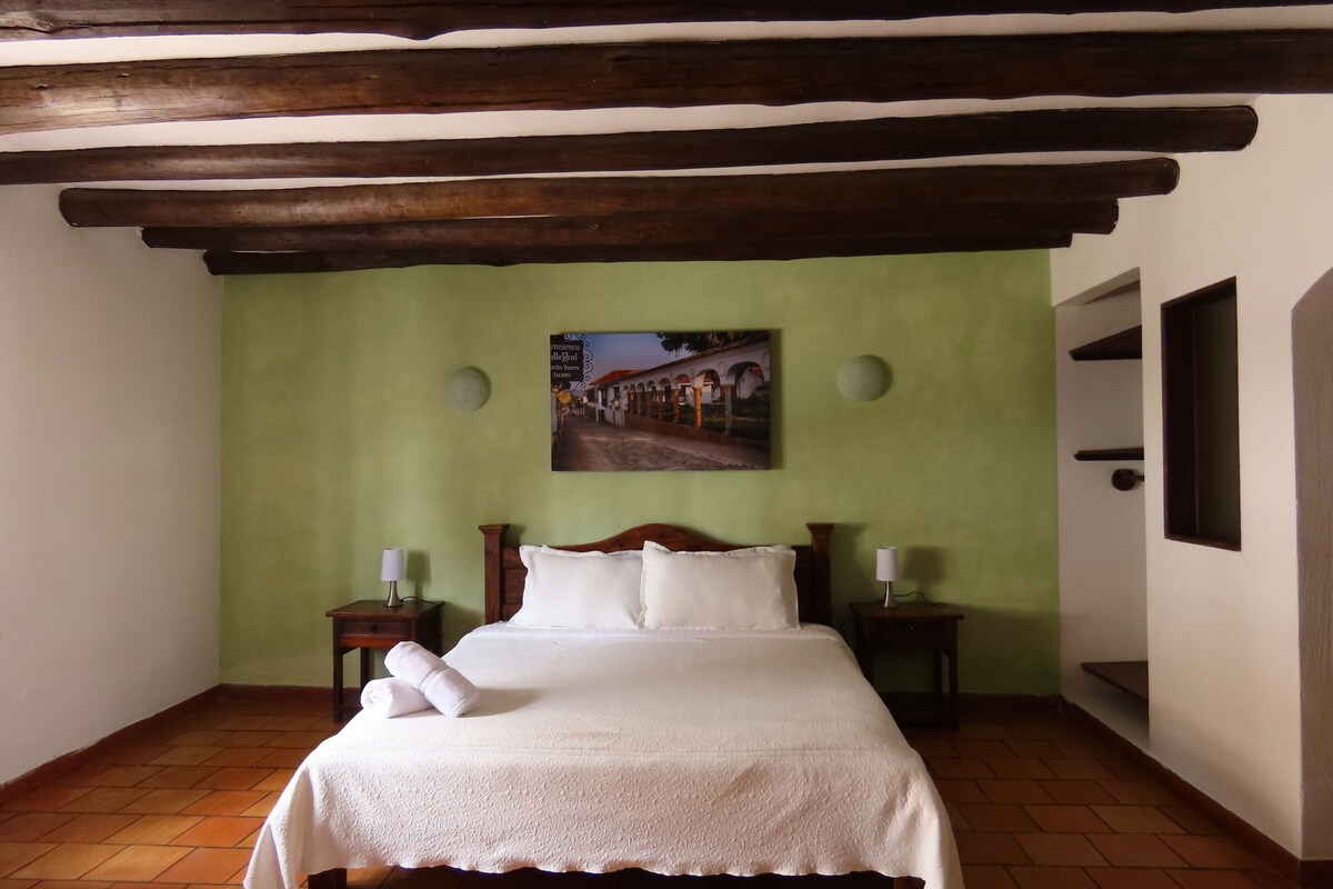 Ein Schlafzimmer mit einem Bett, einem Gemälde, einer grünen Wand und einer Holzbalkendecke.