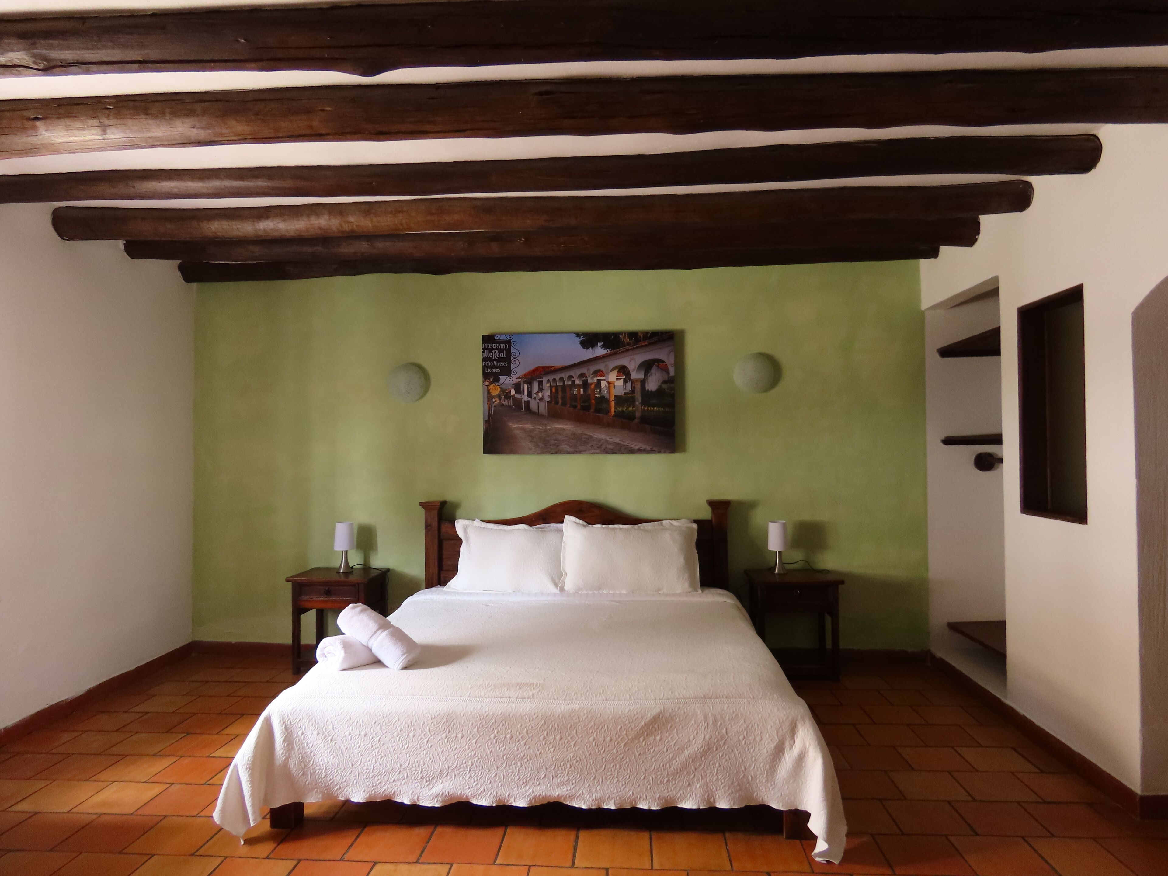 A bedroom with a bed, a painting, a green wall, and a wooden ceiling.