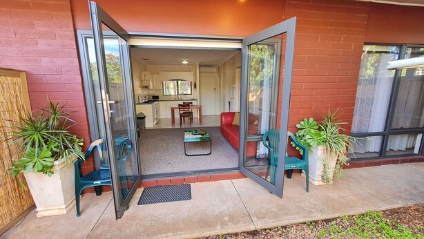 A modern home with a glass door entrance, a living area with a red sofa, a dining table, and a kitchen visible through the door.