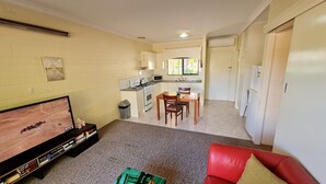 A compact living space with a kitchenette, a dining area, and a seating area with a TV and bookshelf.