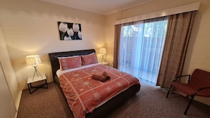 A hotel room with a bed, two bedside lamps, a window with curtains, a chair, and a wall painting.