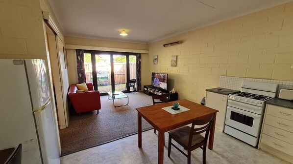 A compact kitchen with a dining area, a red sofa, and a television. - Rise 'n Shine - Affordable 50sqm Garden Apartment (Port Pirie)
