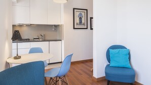 Una cocina moderna con armarios blancos, una zona de comedor con sillas azules y un sillón con cojín azul.
