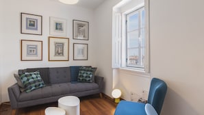 Una sala de estar con un sofá gris, un sillón azul y una ventana con vistas.