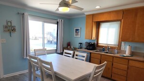 A kitchen with a dining table and chairs, wooden cabinets, a ceiling fan, and a window with curtains.
