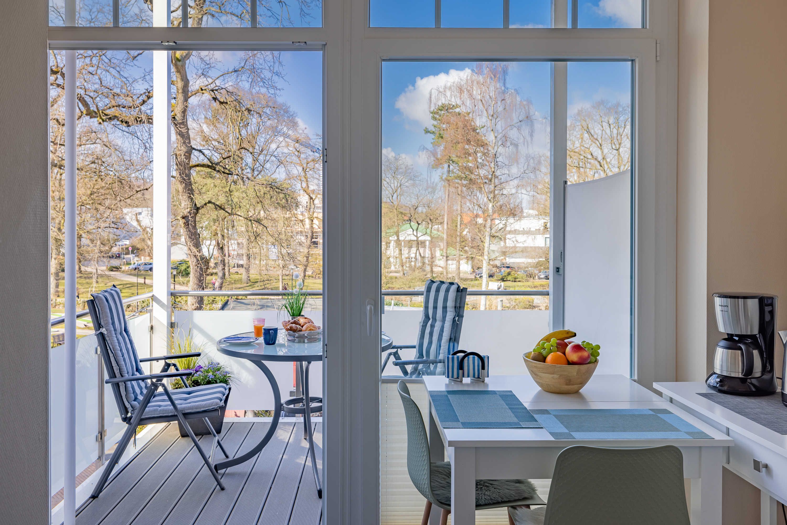 A balcony with a table, chairs, a coffee maker, and a bowl of fruit.