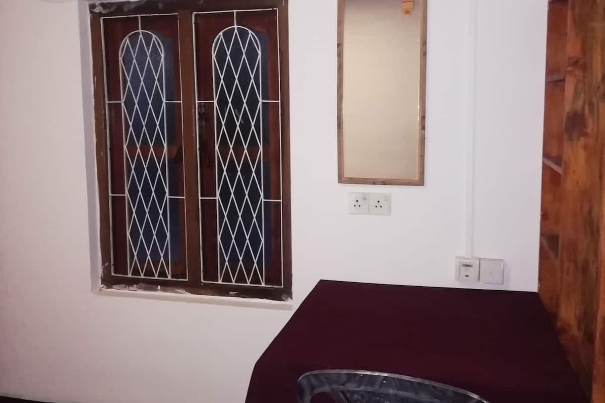 Ein Zimmer mit einem Fenster mit Gitterstäben, einer Wand-Klimaanlage, einem Spiegel und einem Tisch mit roter Tischdecke.