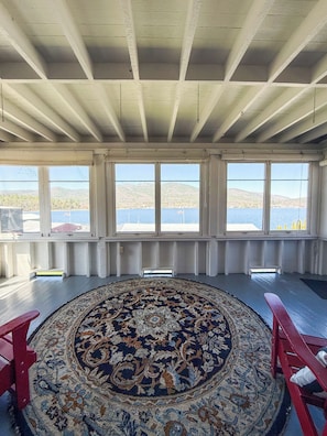 A room with a large rug, wooden beams, and large windows overlooking a body of water. - Lake George Crawford House (Lake George)