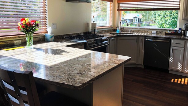 A modern kitchen with granite countertops, a gas stove, a dishwasher, and wooden cabinets.