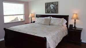 A bedroom with a large bed, two bedside tables with lamps, a window with blinds, and a painting on the wall.